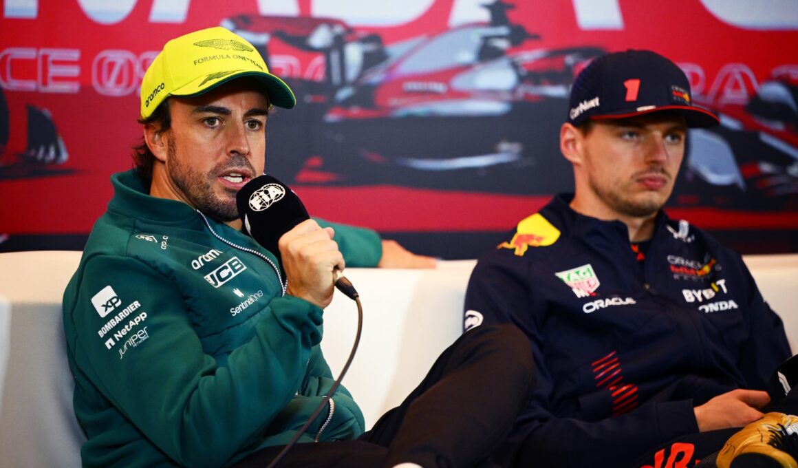 Fernando Alonso talking at a press conference with Max Verstappen in the background