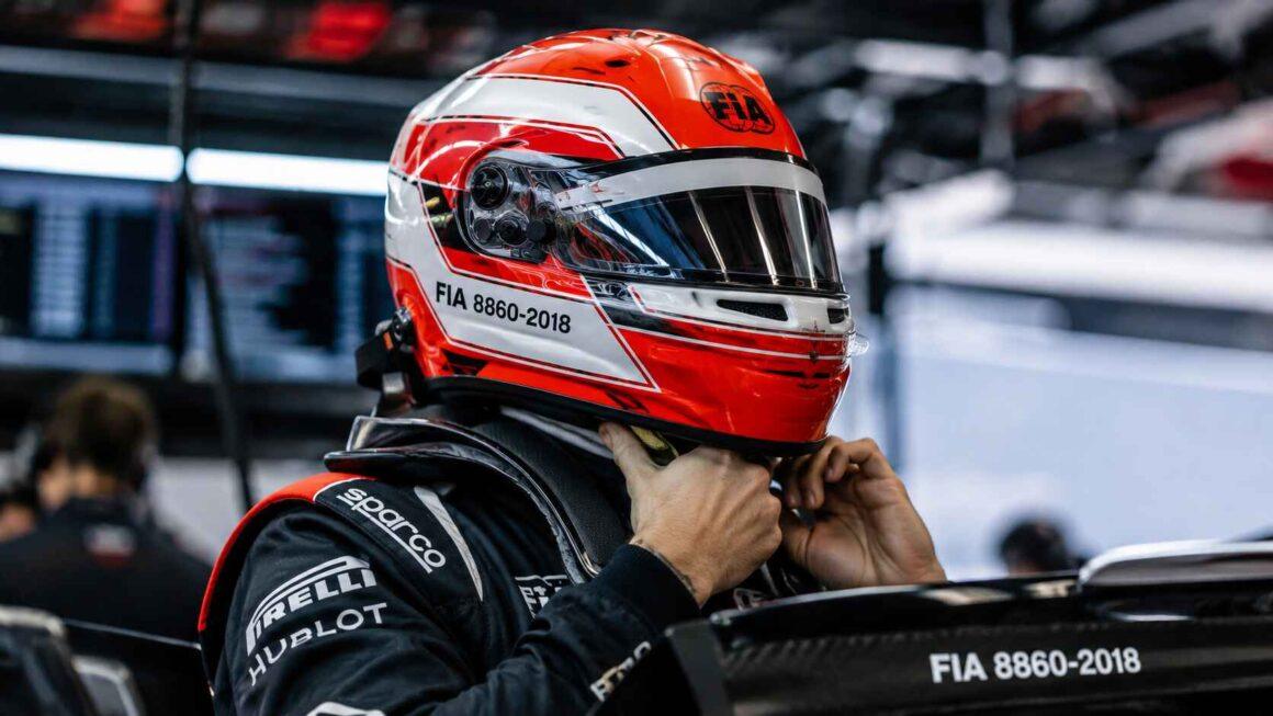 Vue rapprochée d'un pilote en combinaison Sparco, Hublot, Pirelli ajustant son casque rouge et blanc marqué FIA 8860-2018.